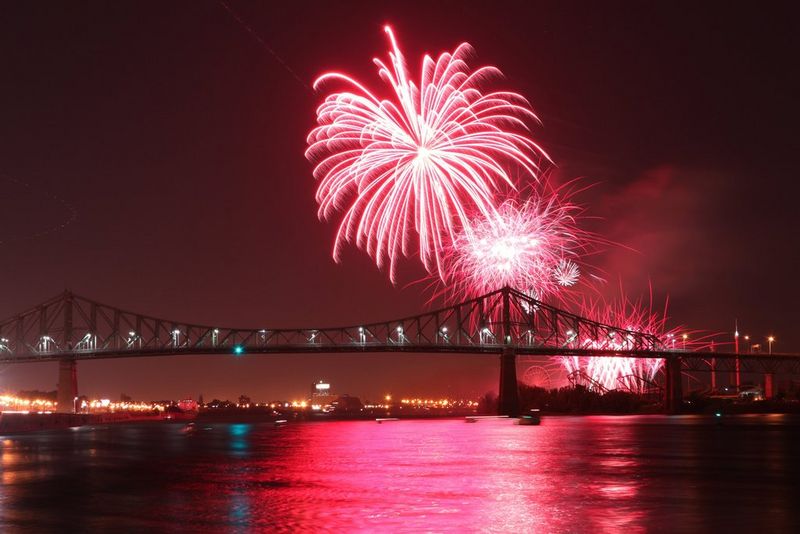 Pink fireworks burst in the night sky over a bridge.