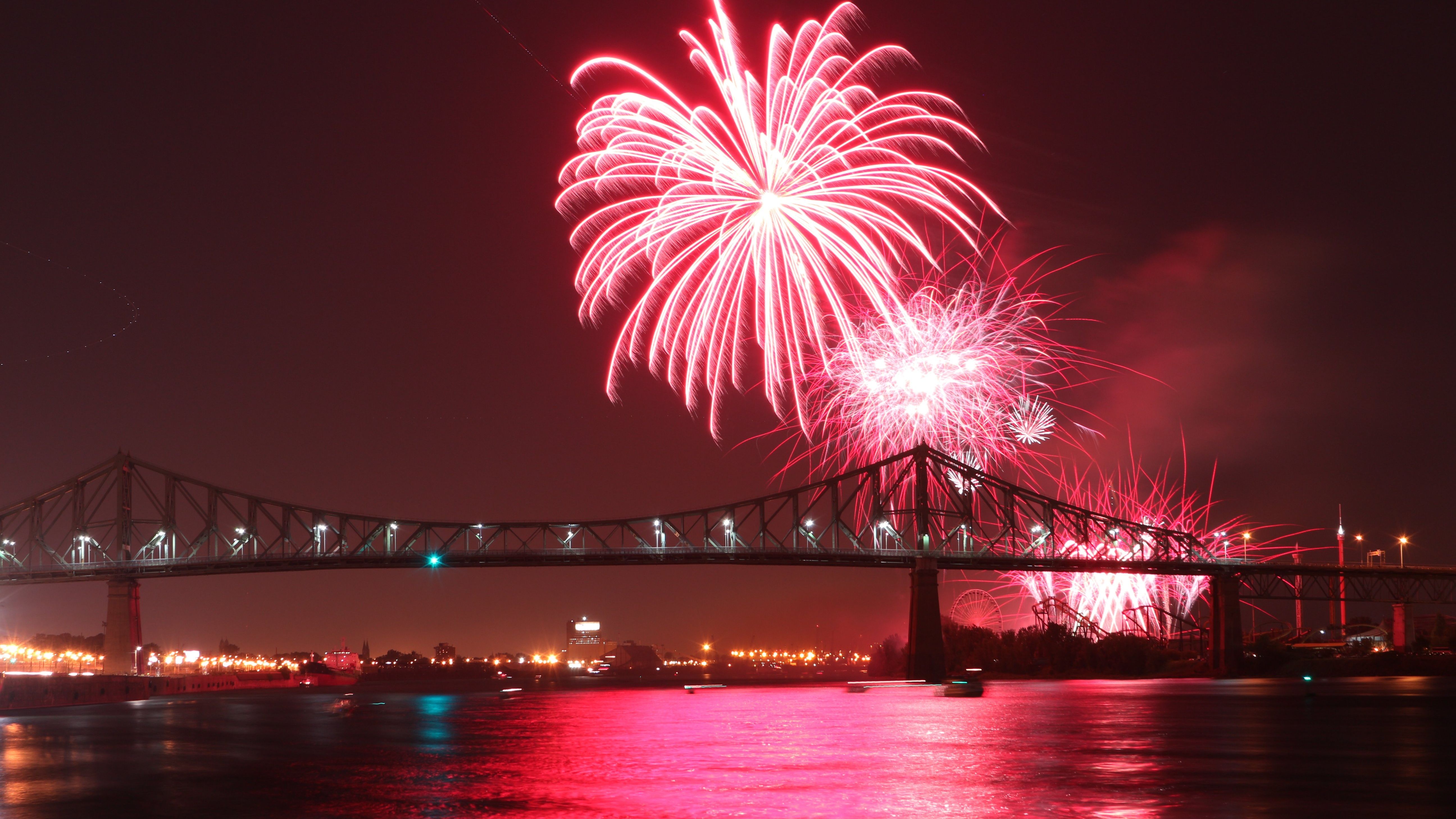 Pink fireworks burst in the night sky over a bridge.