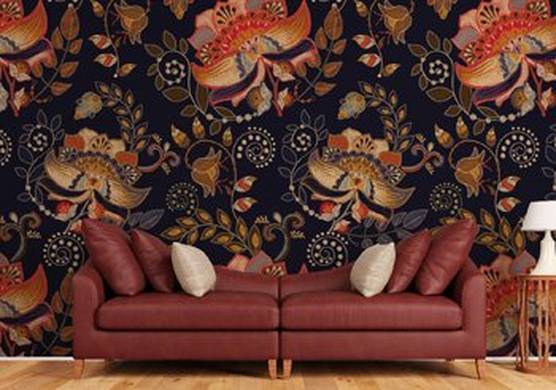 A brown leather sofa and cushions with an occasional table and a lamp to the right. Behind is wallpaper in a repeating design of orange, black and brown leaves and flowers in a modern brocade style, often seen in furnishings and wall coverings.