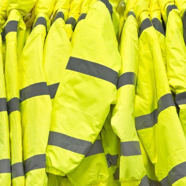 Ten high-visibility fluorescent yellow jackets, hanging closely side by side. They have grey reflective strips at the elbow, wrist and shoulder.