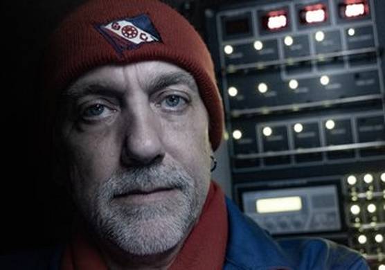 A ‘selfie’ of explorer Richard Garriott. He has a grey beard, blue eyes and an earring in his left-hand ear. He wears a red hat and scarf, and a blue jacket, of which only the shoulder is pictured. Behind him are the control panels of the submersible DSV Limiting Factor, with many round white lights. (© Richard Garriott de Cayeux, using Canon EOS R / Canon RF24-105mm F4 IS USM)