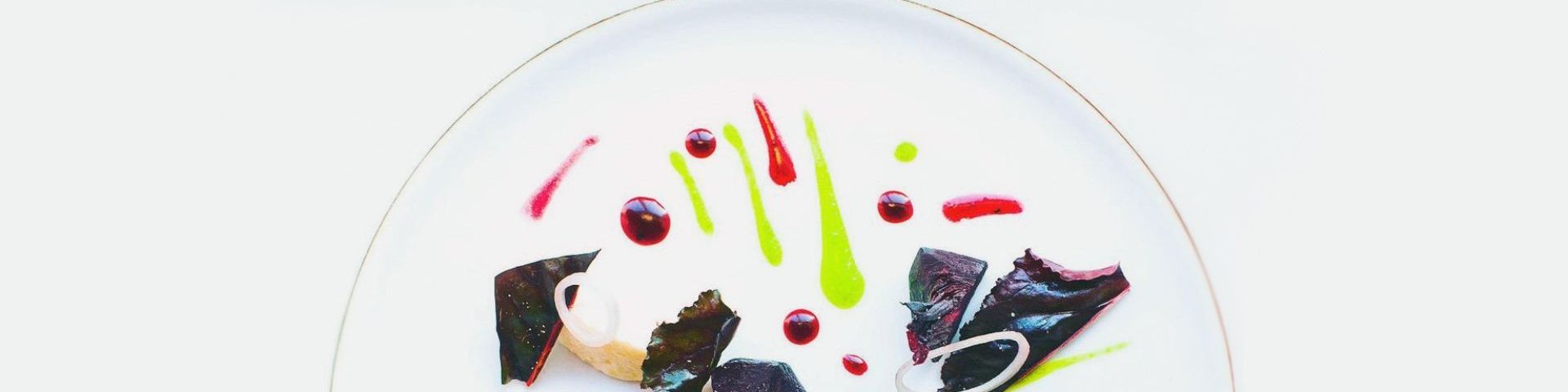 A red chard, beetroot, plant ricotta and parsley dish. Only the top half of the gold-trimmed white plate is shown and sits as a semicircle in the middle of the photo. The sauces of the dish are spotted and striped on the plate in bright pinks and vivid lime green.