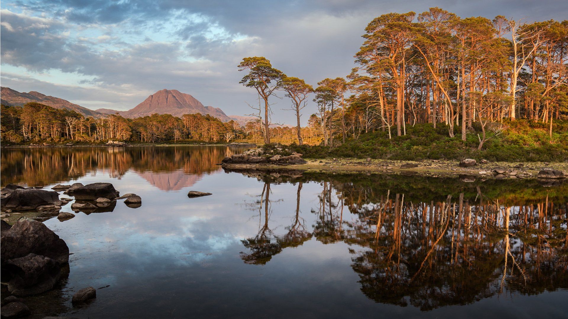 Trees reflect in a lake in Scotland with a mountain in the background