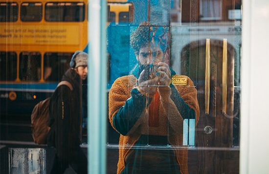 Giuseppe Esposito-Rodrigues taking a photo of a shop window, showing passers by in the reflection.