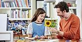 A father and daughter making papercraft flowers.