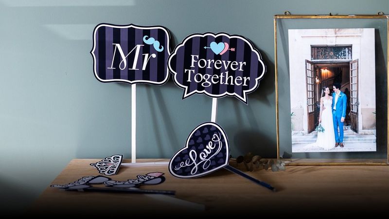 Printed decorations and hand-held signs for a wedding day next to a portrait of a bride and groom in a frame.