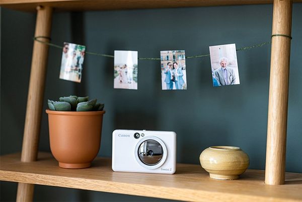 A selection of images displayed on a string above a bookshelf holding a Canon Zoemini S.