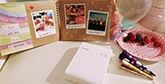 A scrapbook on a table filled with instant camera prints with a Canon Selphy Square QX10 printer.