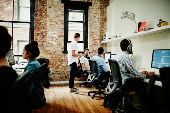 Colleagues working on computers in a shared office space with exposed brick and wooden floor