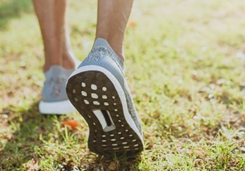 A pair of feet in running shoes, walking across grass.
