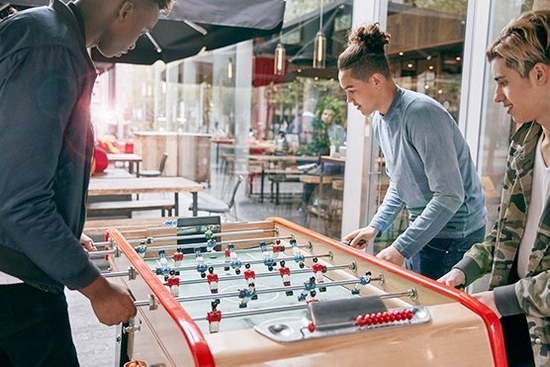 Three people play table football in a communal space