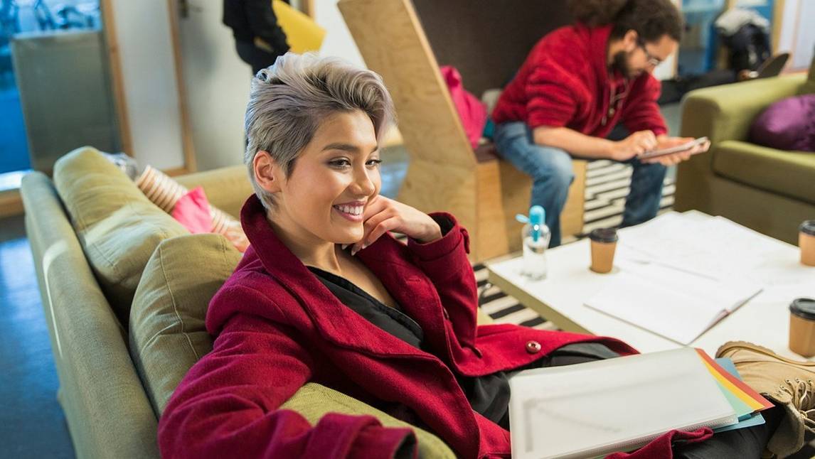 Short-haired woman in red jacket smiles from sofa