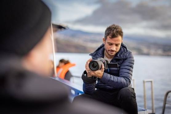 A man sat on the edge of a boat filming with a Canon EOS R5 C camera. 
