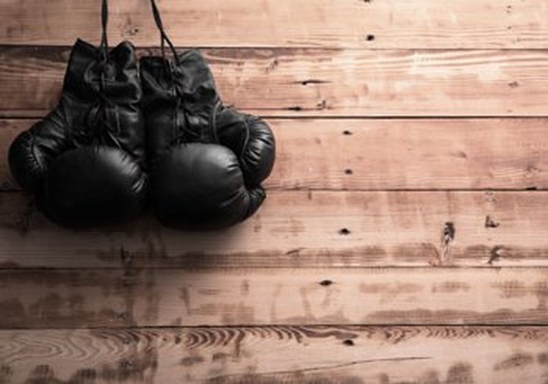 A pair of old-fashioned black lace-up boxing gloves, lying against a wooden background.