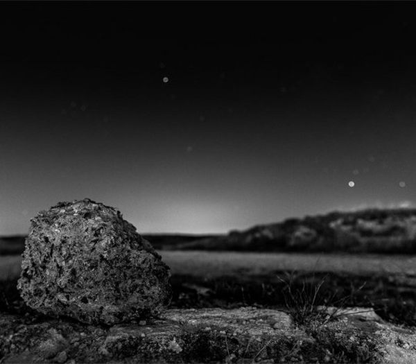 A barren black and white landscape, with a large rock in the foreground.
