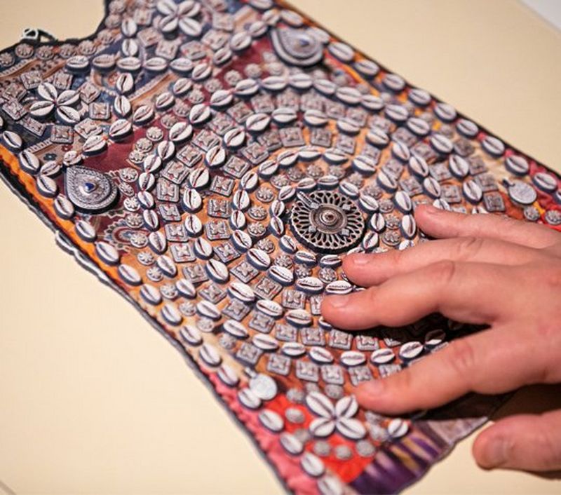 A hand touches a reproduction of a piece of indigenous artwork. 