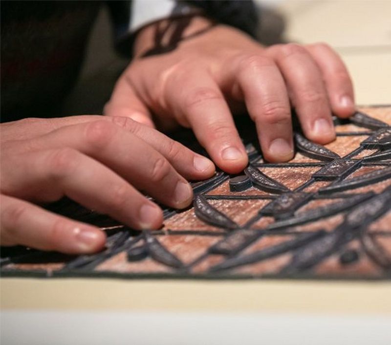 Two hands feeling a reproduction of a piece of indigenous artwork.