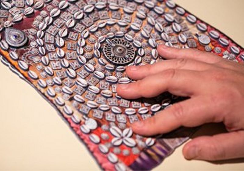 A hand touches a reproduction of a piece of indigenous artwork. 