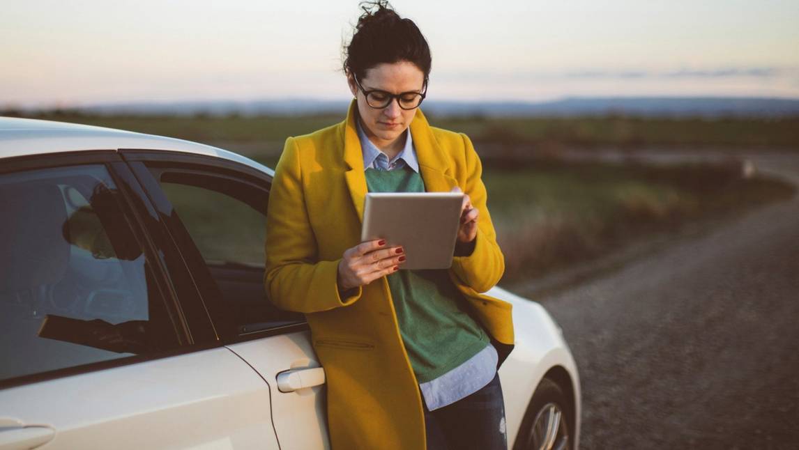 Woman on tablet leaning on car 