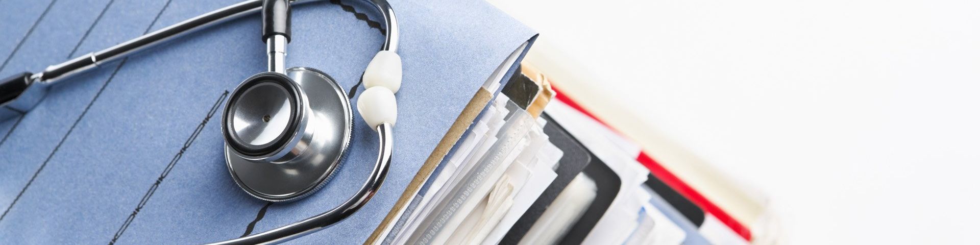 A stethoscope on top of a pile of folders full of paper. 
