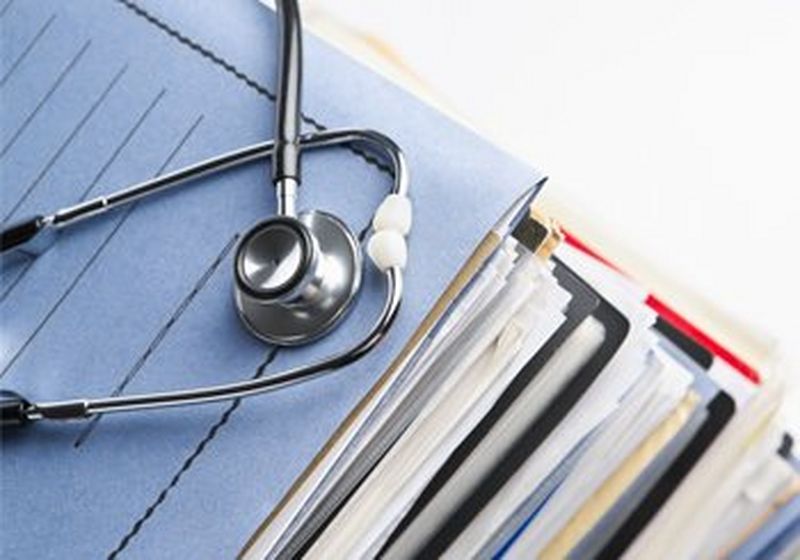 A stethoscope on top of a pile of folders full of paper.