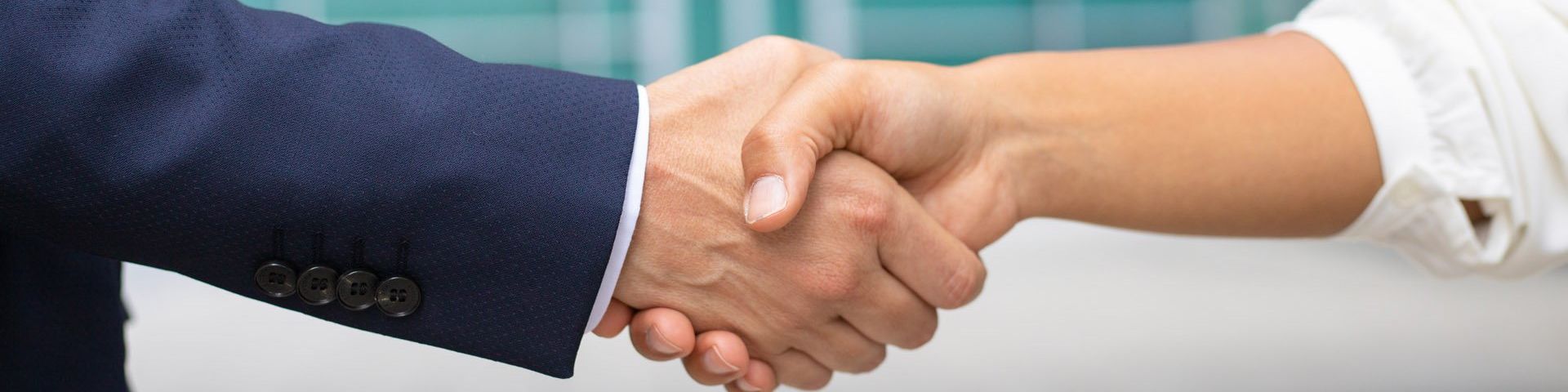 A close up of a handshake between someone wearing a blue suit and a white shirt.