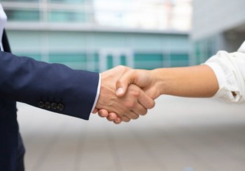 A close up of a handshake between someone wearing a blue suit and a white shirt.