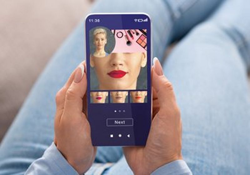A pair of hands holds a smartphone, which is running an app that allows you to scan your own face and try out different lipstick colours.