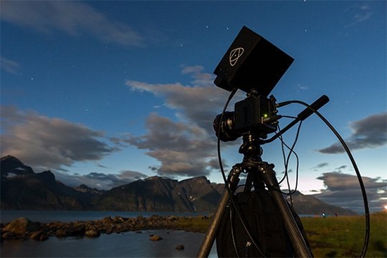 A Canon ME20F-SH cinema camera attached to a tripod beside a mountain lake.
