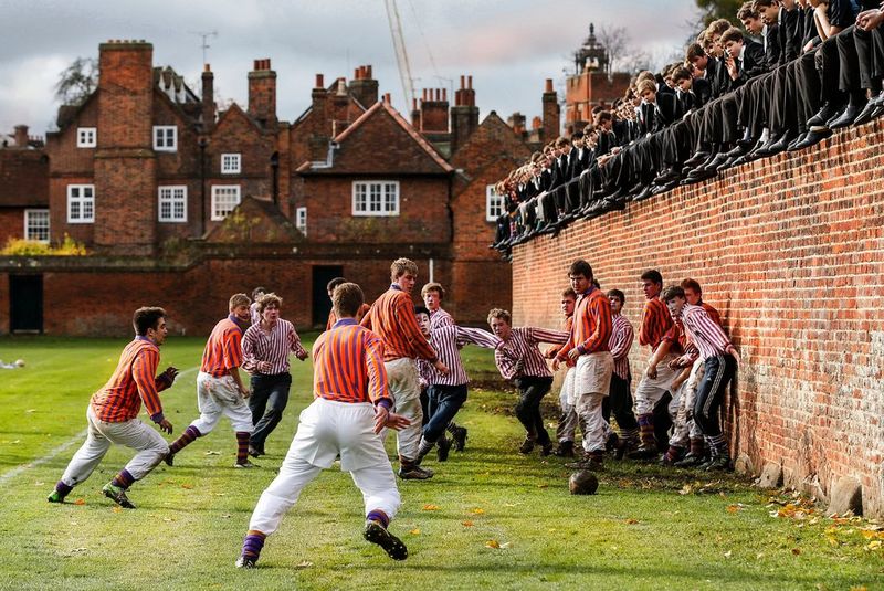 Pupils at Eton College play football dressed in traditional attire and watched by other pupils from a wall above. Photo by Canon Ambassador Eddie Keogh.