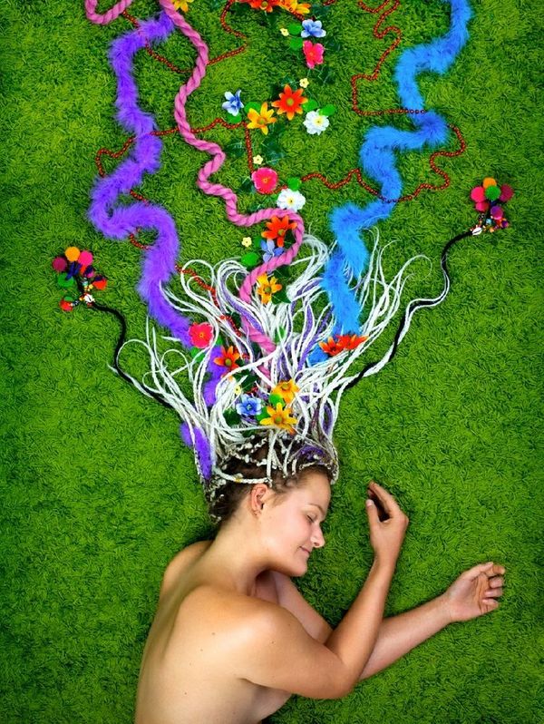 A still from a video self-portrait of Neoza Goffin. She is lying on grass with colourful ribbons in her hair.