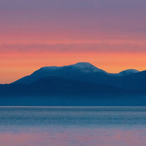 The sky is streaked orange and pink behind the outline of Ben Nevis in the Highlands, Scotland. 