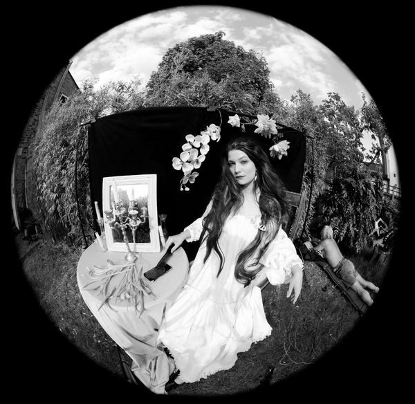 A black-and-white image shot with a fisheye lens of Wanda Martin recreating Dante Gabriel Rossetti's Lady Lilith in her garden.