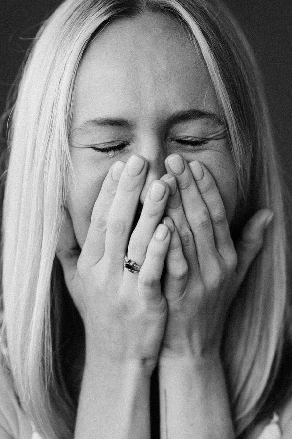 A black-and-white portrait of a woman crying, her face in her hands.