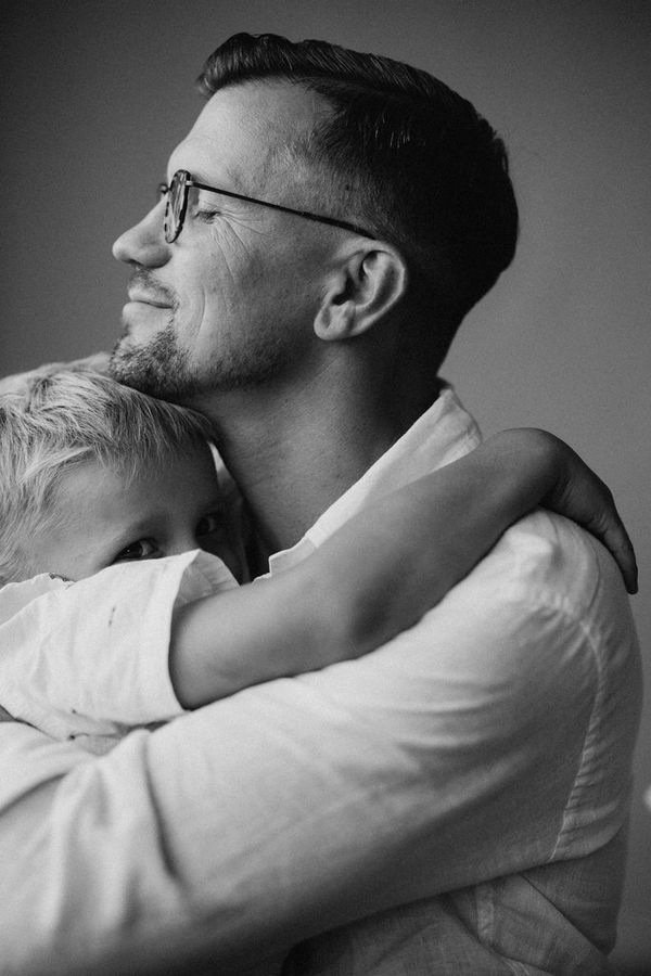 A black-and-white portrait shot of a father and son embracing.