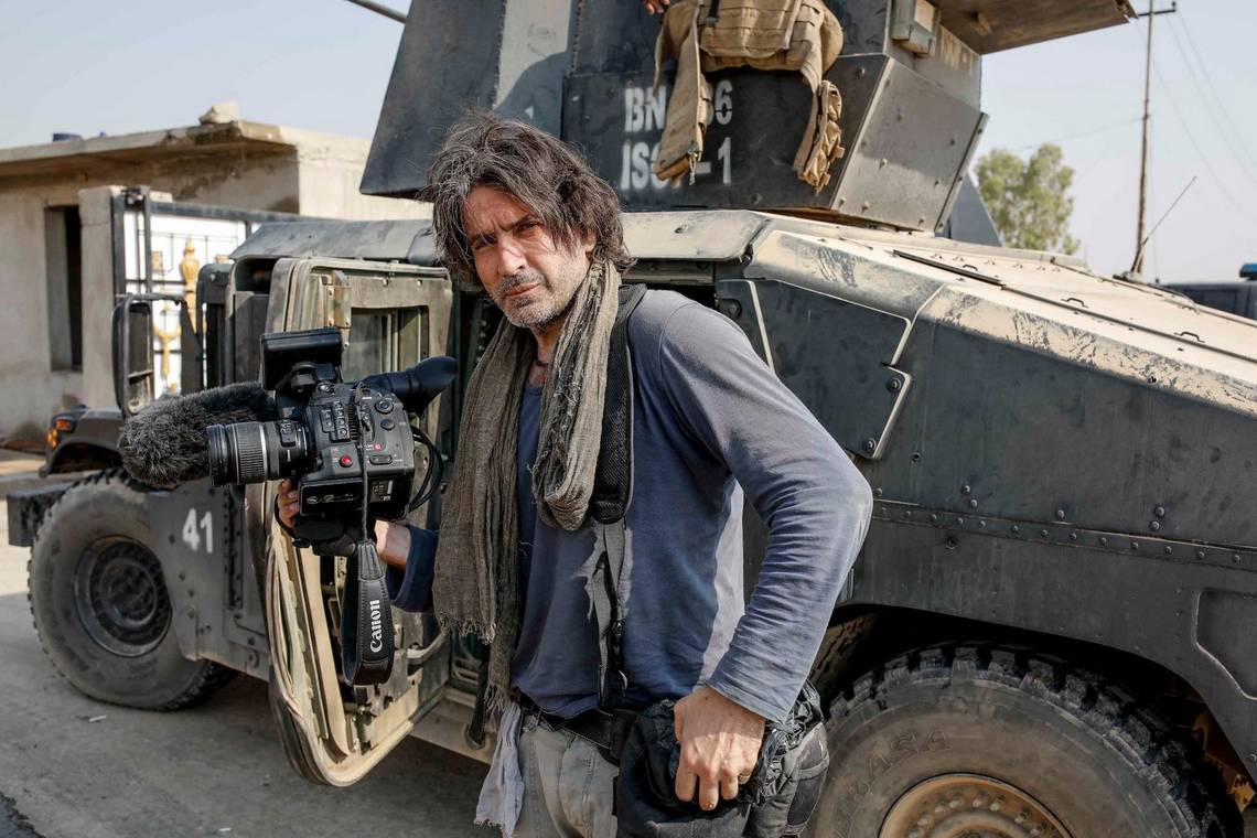 Filmmaker Olivier Sabril standing in front of a tank in Mosul, Iraq, with a Canon EOS C300 Mark II video camera.