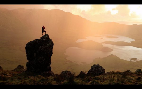 A video still of a figure atop a rocky outcrop silhouetted against the landscape, by travel photographer Joel Santos.