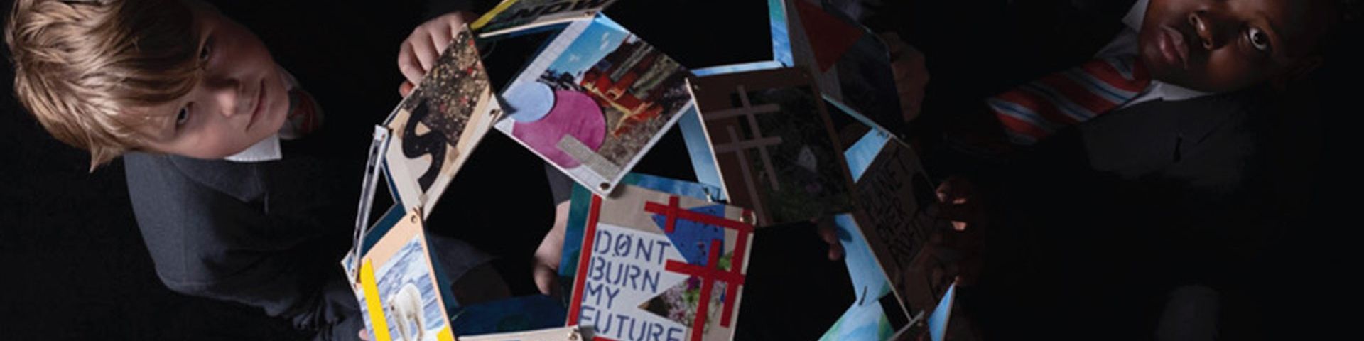 Taken from above, two children, on the left and right of the photo, hold a globe made of photographs and raise their solemn faces to the camera. The clearest photo, closest to the camera displays the words ‘don’t burn my future’.