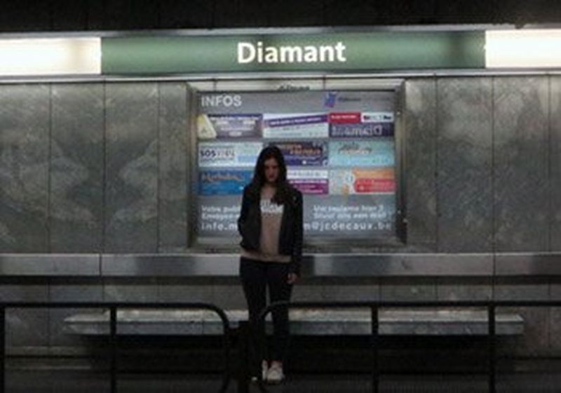 A young woman stands alone on a deserted metro platform.