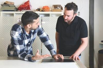 Two men discuss printed material they are looking at on a desk
