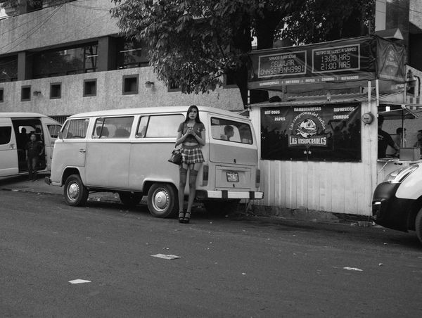 A young woman stands by parked cars on a street.