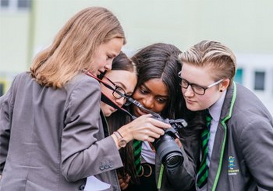Four students in school uniform look at the rear display on a Canon camera