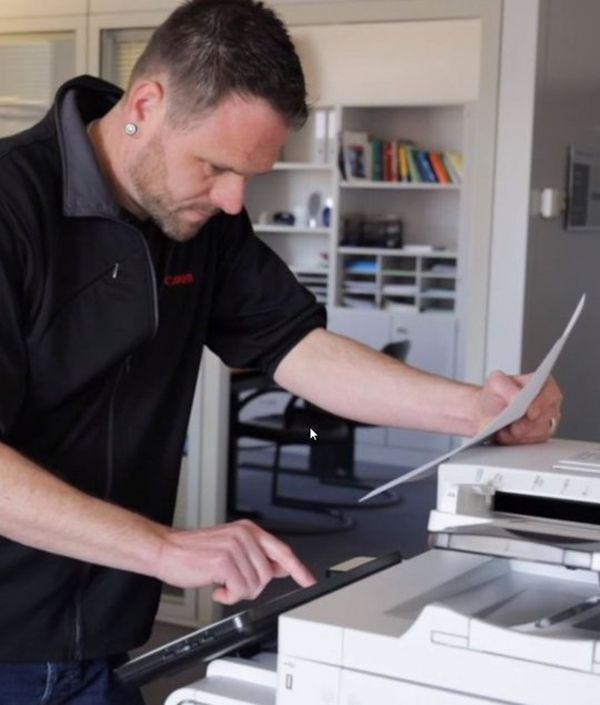 A Canon service engineer holds a piece of paper and inputs some information into a business machine.