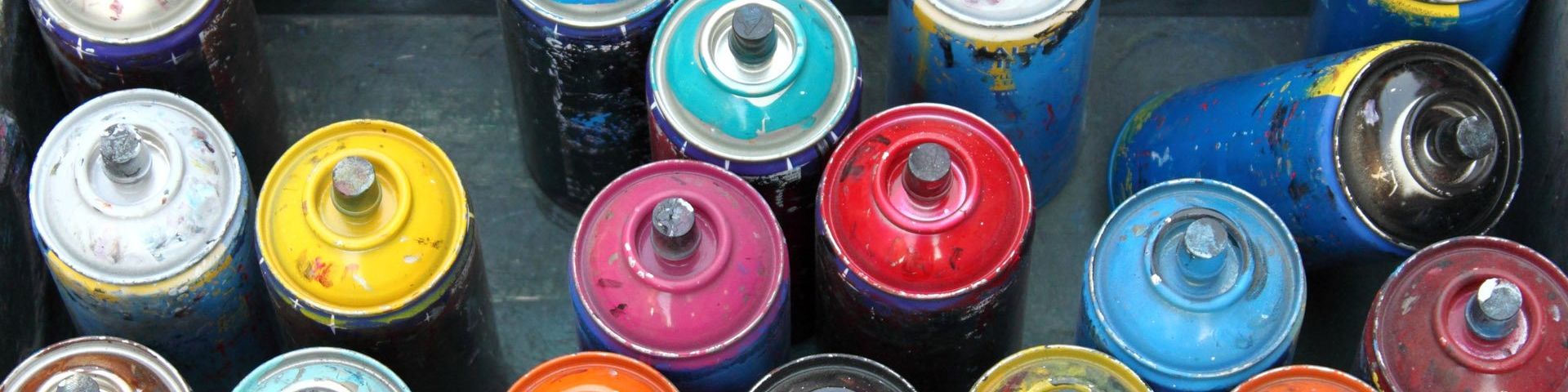 An image taken from above of eighteen used spray cans of different colours.