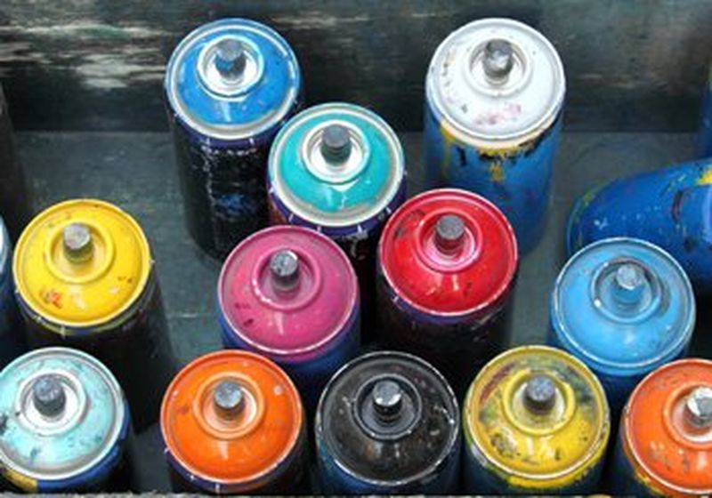 An image taken from above of thirteen used spray cans of different colours.