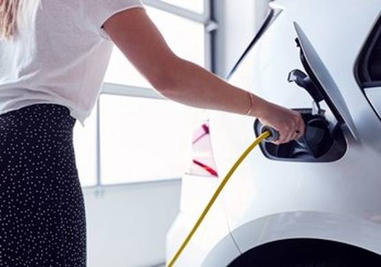 A woman in a polka dot skirt and white t-shirt charges her white electric vehicle.