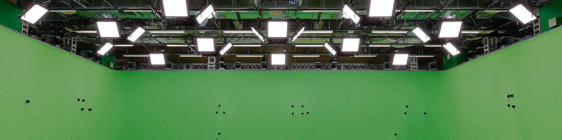 The ceiling and walls of the new Canon Volumetric Video studio in Kawasaki, Japan. The walls are green and have small, round black objects protruding from them at seemingly random positions and intervals. Above are more than two dozen flat square lights hanging from a rig below the ceiling.