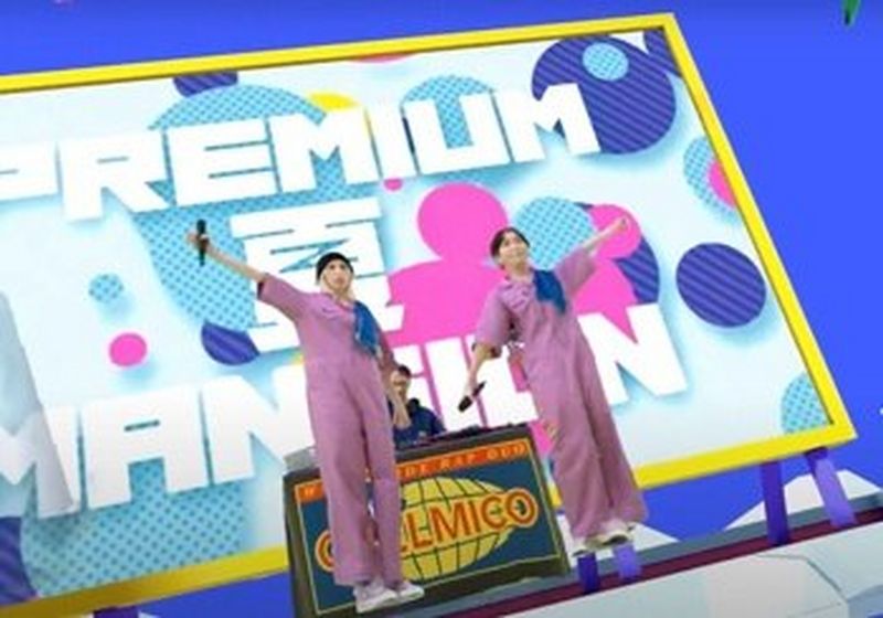 Two women in lilac jumpsuits stand against a colourful backdrop. They each have an arm outstretched. Behind them is a man standing behind a DJ booth that is labelled ‘chelmico’. © Warner Music Japan Inc. 