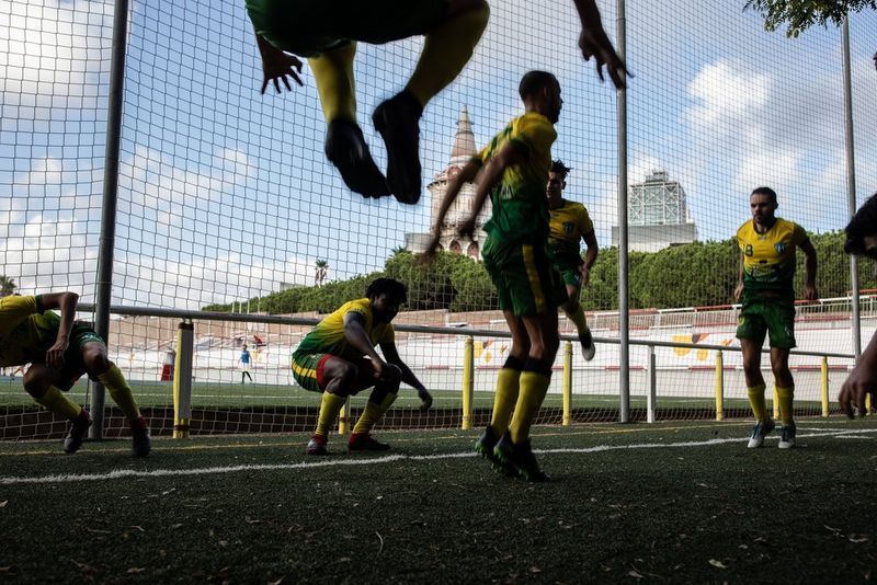 Grupo de jugadores vestidos de amarillo y verde durante un ejercicio de entrenamiento. Uno está en pleno salto, mientras que otros están agachados o a punto de ponerse en cuclillas. Al fondo se ven unas redes, árboles verdes y un cielo parcialmente nublado. Cortesía del proyecto Goals for Change. Creado por Ofelia de Pablo, Javier Zurita y Pablo Tosco.