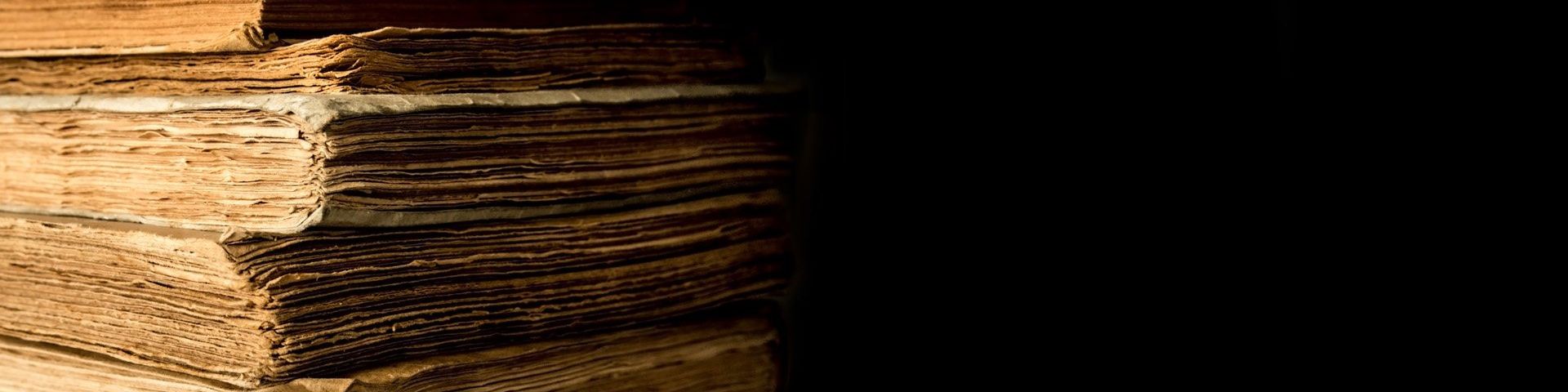 On the left, a stack of very old books, viewed from the leaves not spine. On the right, a black background.